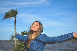 A woman with her arms out looking up in to the sky, outside in the wind, with Yellow NOZ sunscreen on her nose.