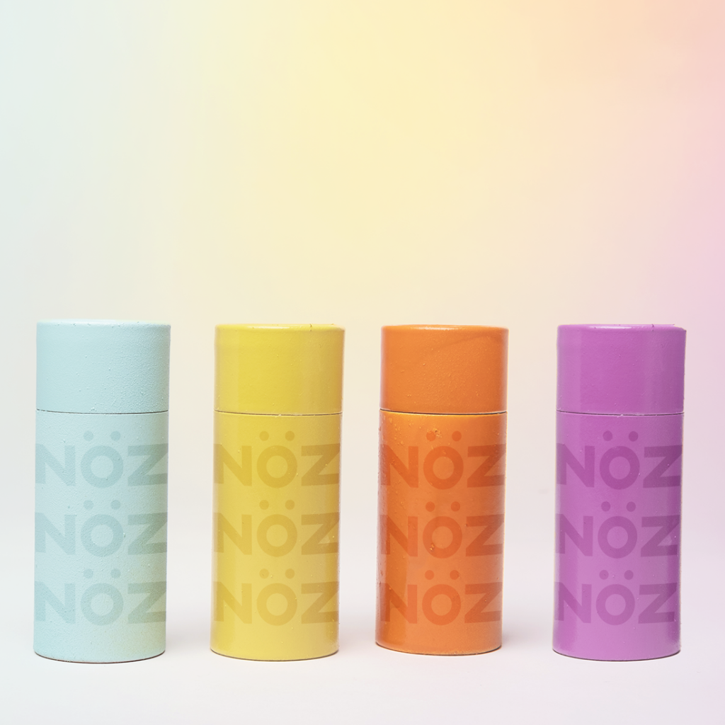 Four colorful sticks of NÖZ sunscreen in blue, yellow, orange, and purple.