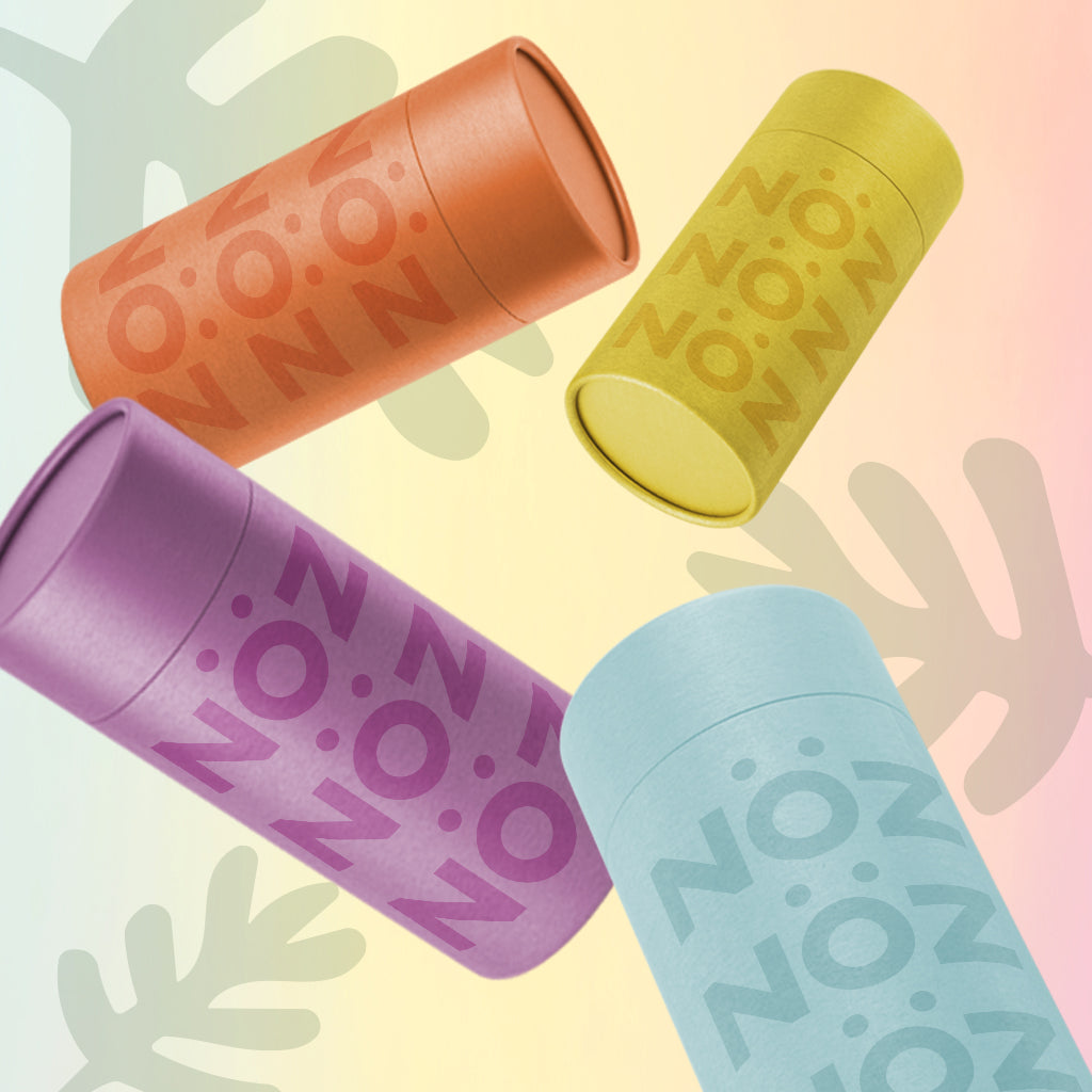 Four sticks of NÖZ sunscreen in the colors orange, yellow, blue and purple floating in the image