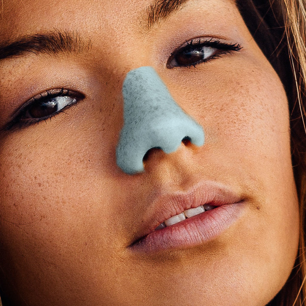 A young woman wearing blue NÖZ sunscreen on her nose.